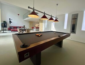 A pool table with a Bison logo, a red sofa, and a dining area with red chairs.