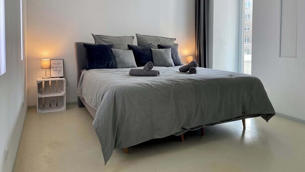 A modern bedroom with a bed, pillows, a bedside table with a lamp, and a window with curtains. - Design Loft with Pool Table for 6 (Berlin)