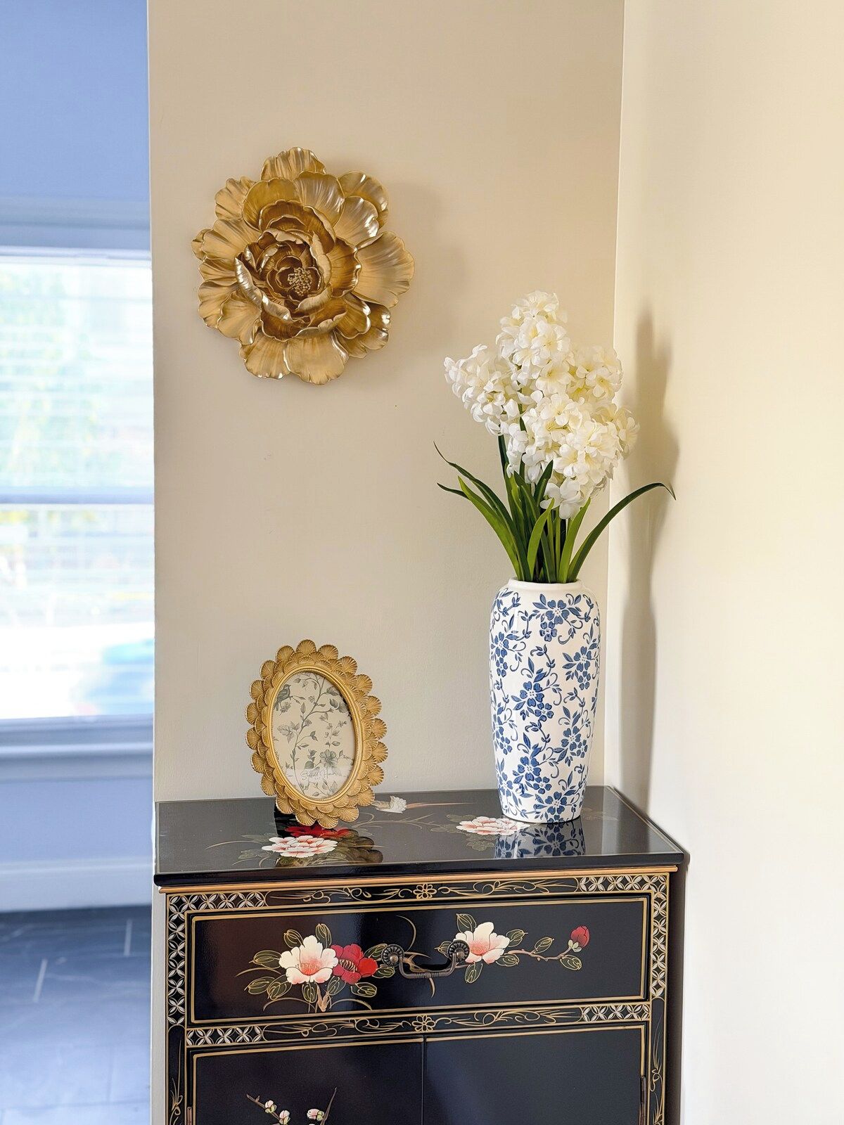A black and gold decorative piece with a vase of white flowers on a table.