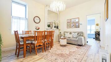 A dining area with a wooden table and chairs, a chandelier, a sofa, and a rug.