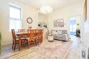 Een eetgedeelte met een houten tafel en stoelen, een kroonluchter, een bank en een vloerkleed.