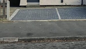 Ett tvåvåningshus med en mörk ytterdörr, en liten veranda och en asfalterad uppfart.