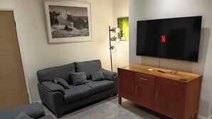 Ett vardagsrum med en grå soffa, ett TV-bord i trä, en inramad tavla och en golvlampa.