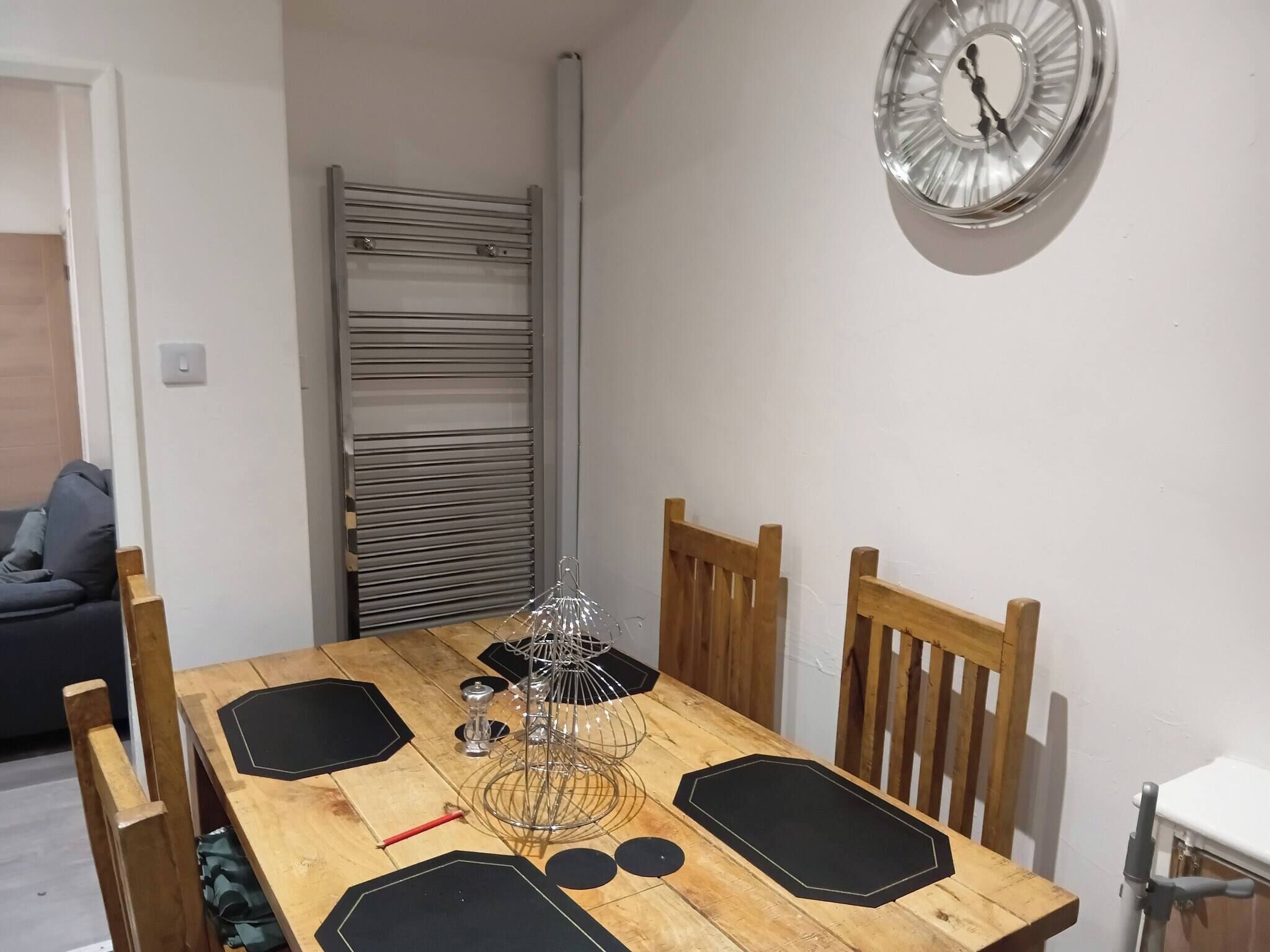 A dining area with a wooden table, chairs, a metal rack, a clock, and a radiator.