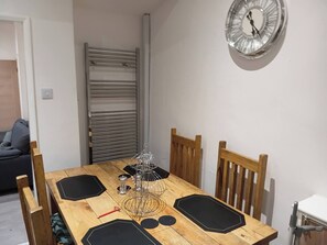 A dining area with a wooden table, chairs, a metal rack, a clock, and a radiator. - Dale Combe is a mid Terrace House (Manchester)