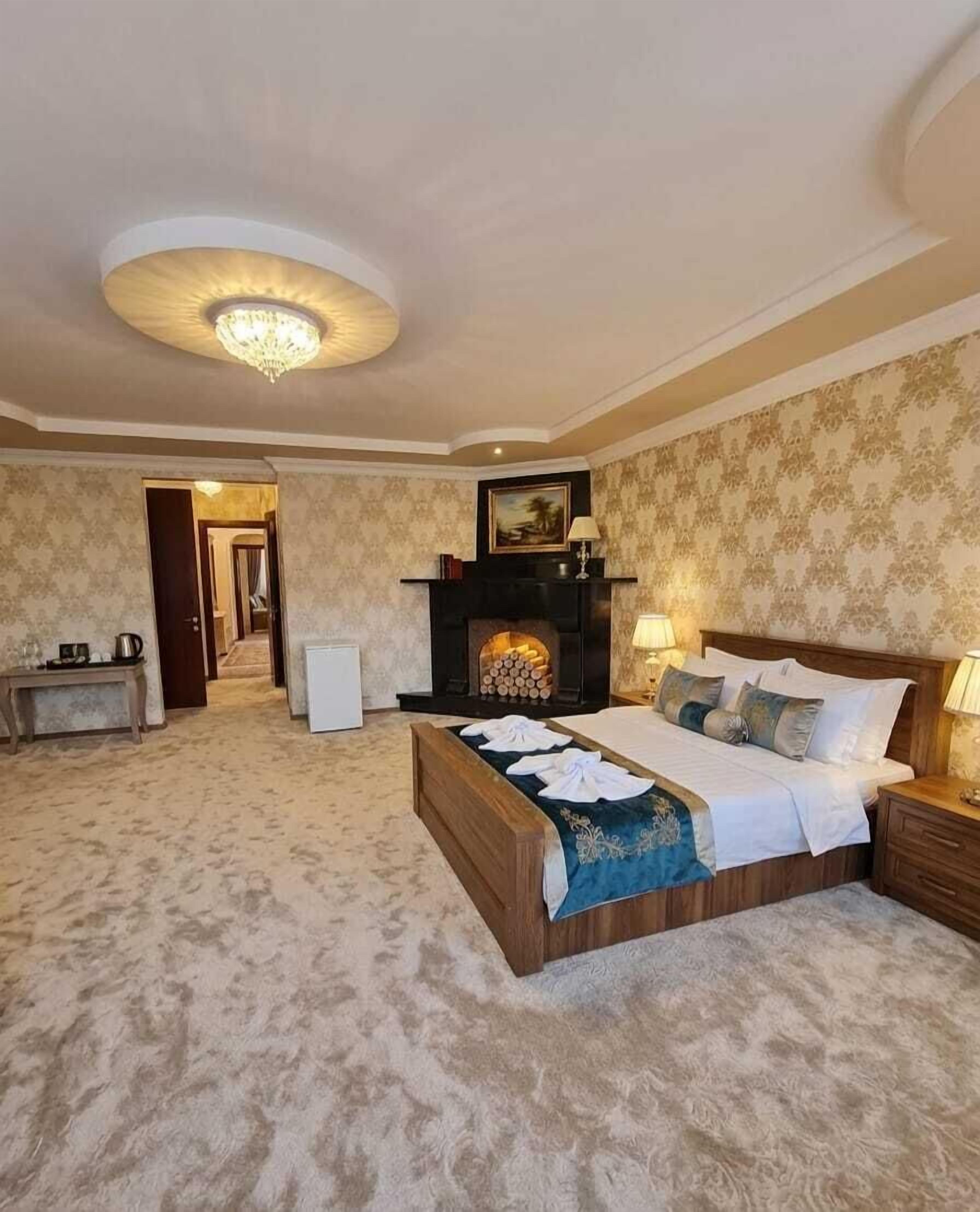 A bedroom with a bed, a fireplace, a chandelier, and a door leading to another room.