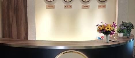 A reception desk with clocks labeled with city names, a logo, and a potted plant.