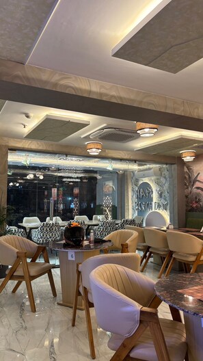 A restaurant interior with modern decor, marble flooring, and a view of the cityscape through large windows. - BKRS Hotel (Varanasi)