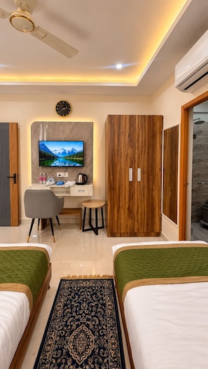 A hotel room with two beds, a desk with a TV, a wardrobe, and a ceiling fan. - BKRS Hotel (Varanasi)