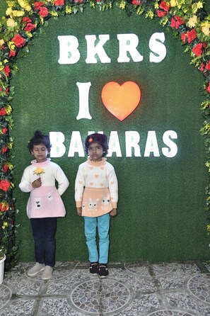 Due bambini in piedi davanti a un muro verde con il testo 'BKRS I ♥ BARAAS' e un simbolo a forma di cuore.