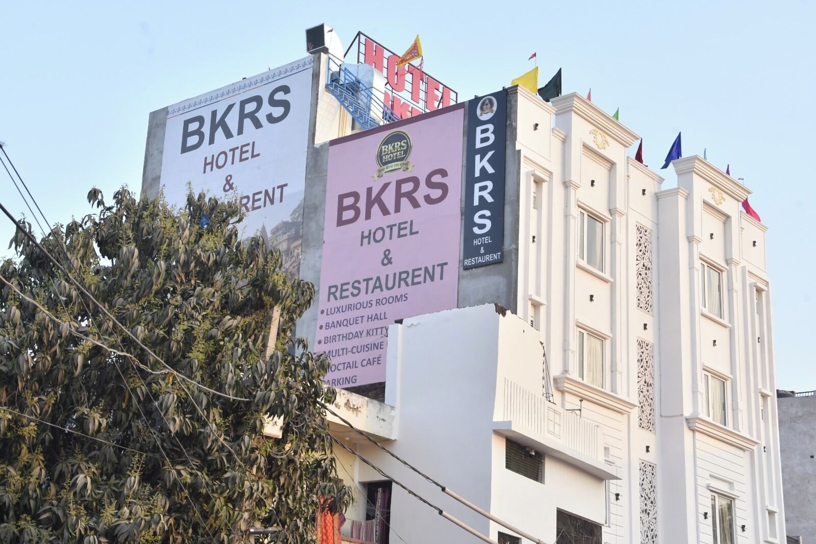 A hotel with signage for 'BKRS HOTEL & RESTAURANT' and 'BKRS HOTEL & RESTAURANT' with amenities listed including 'LUXURIOUS ROOMS,' 'BANQUET HALL,' 'BIRTHDAY KITTY,' 'MULTI-CUISINE,' and 'HOTTAIL CAFÉ.'