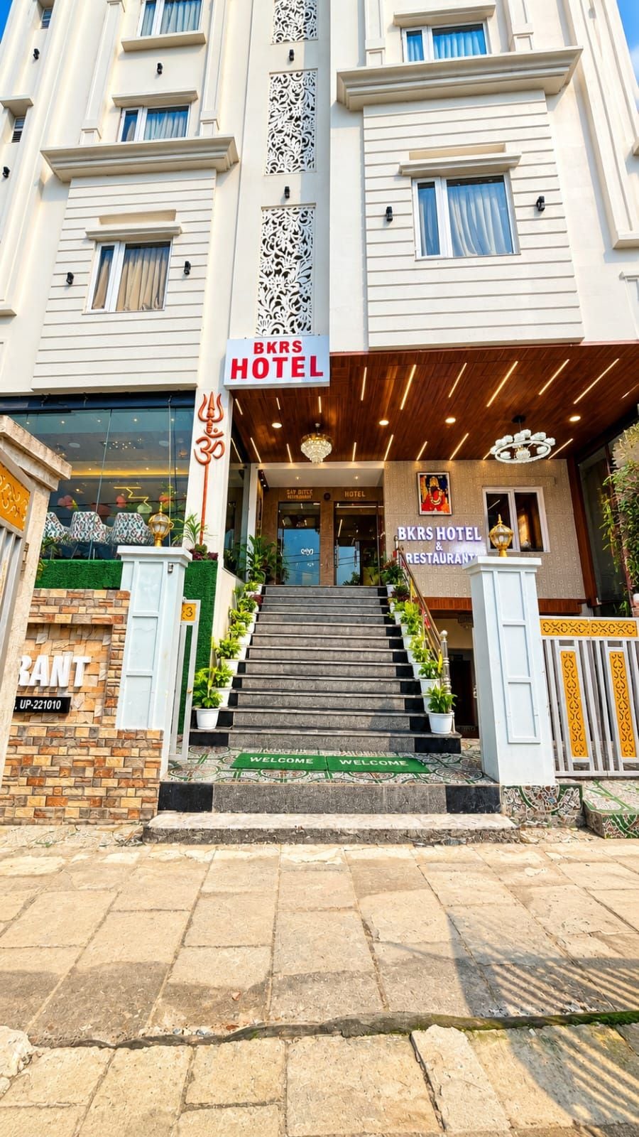 A hotel entrance with a staircase leading to the lobby, a signboard for the hotel, and a welcome mat.