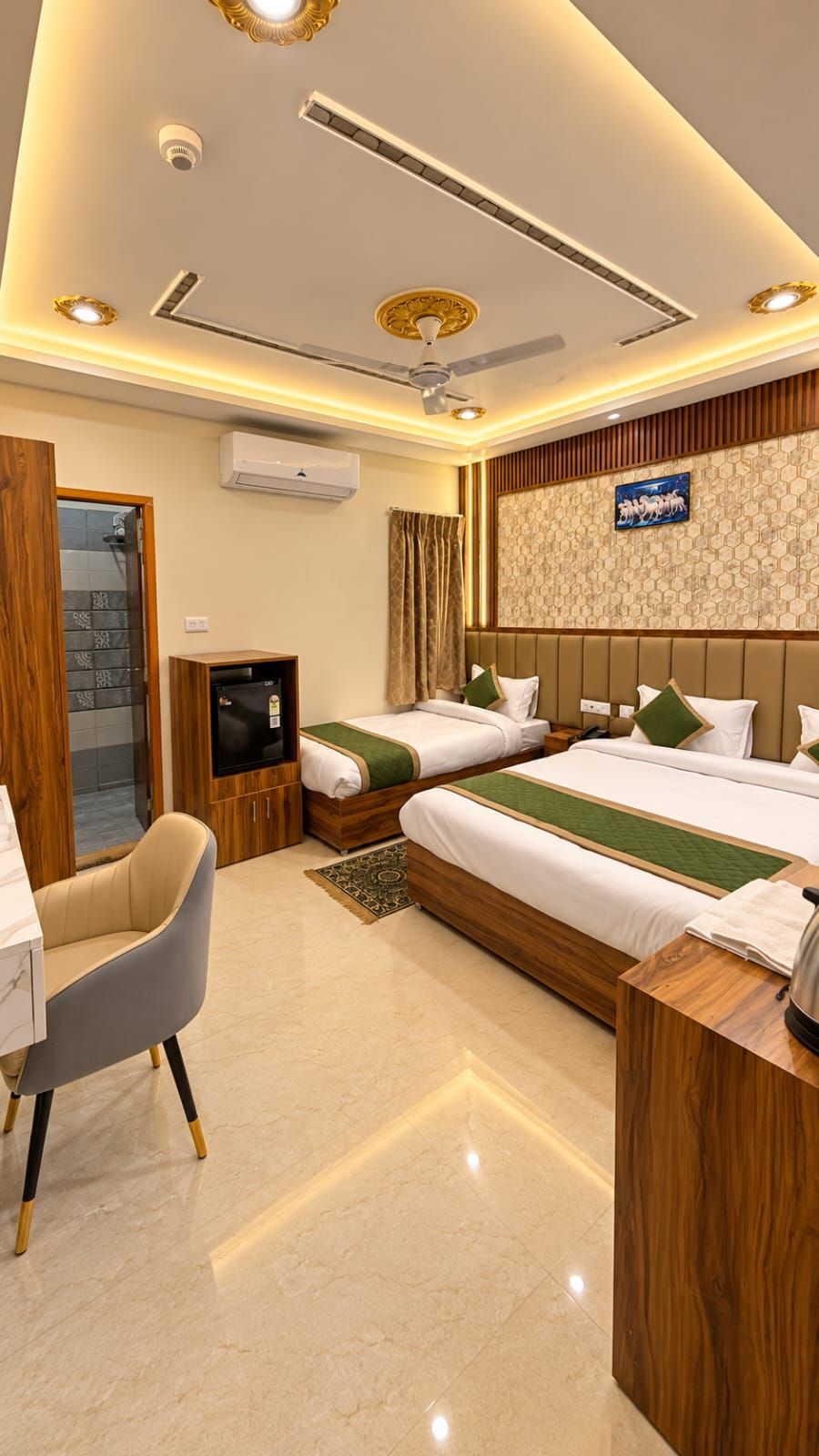 A hotel room with two beds, a desk, a chair, a television, and a ceiling fan.