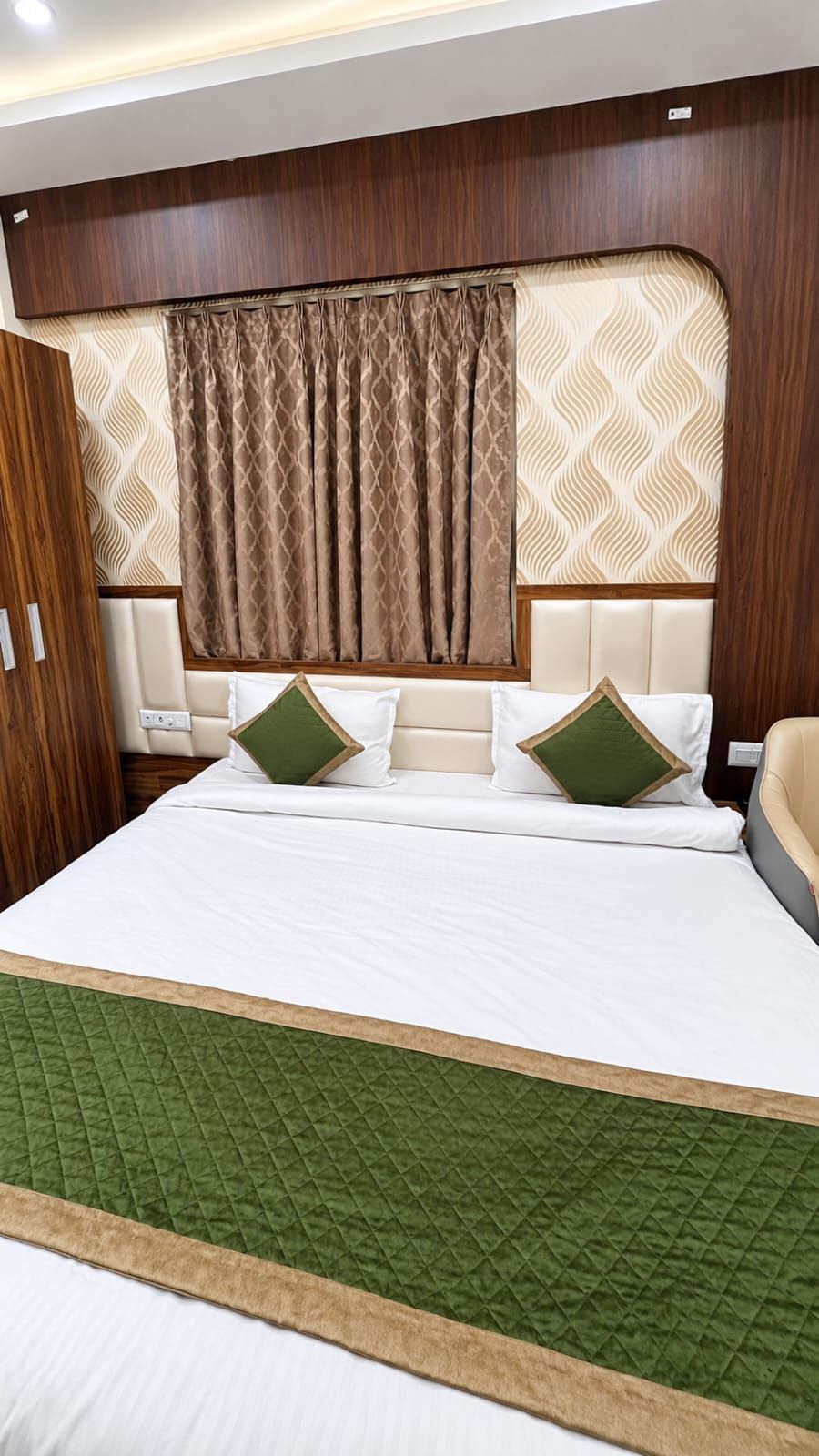 Una habitación de hotel con una cama grande, cabecera con diseño estampado y colcha verde acolchada.