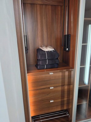 A wooden wardrobe with a mirror, a hanging rack, and a folded towel on the top shelf.