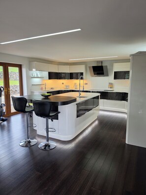 A modern kitchen with a central island, bar stools, and a stone wall visible through the door.