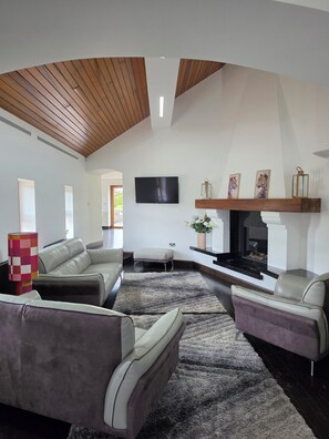 A modern living room with a fireplace, leather sofas, a flat-screen TV, and a wooden ceiling.