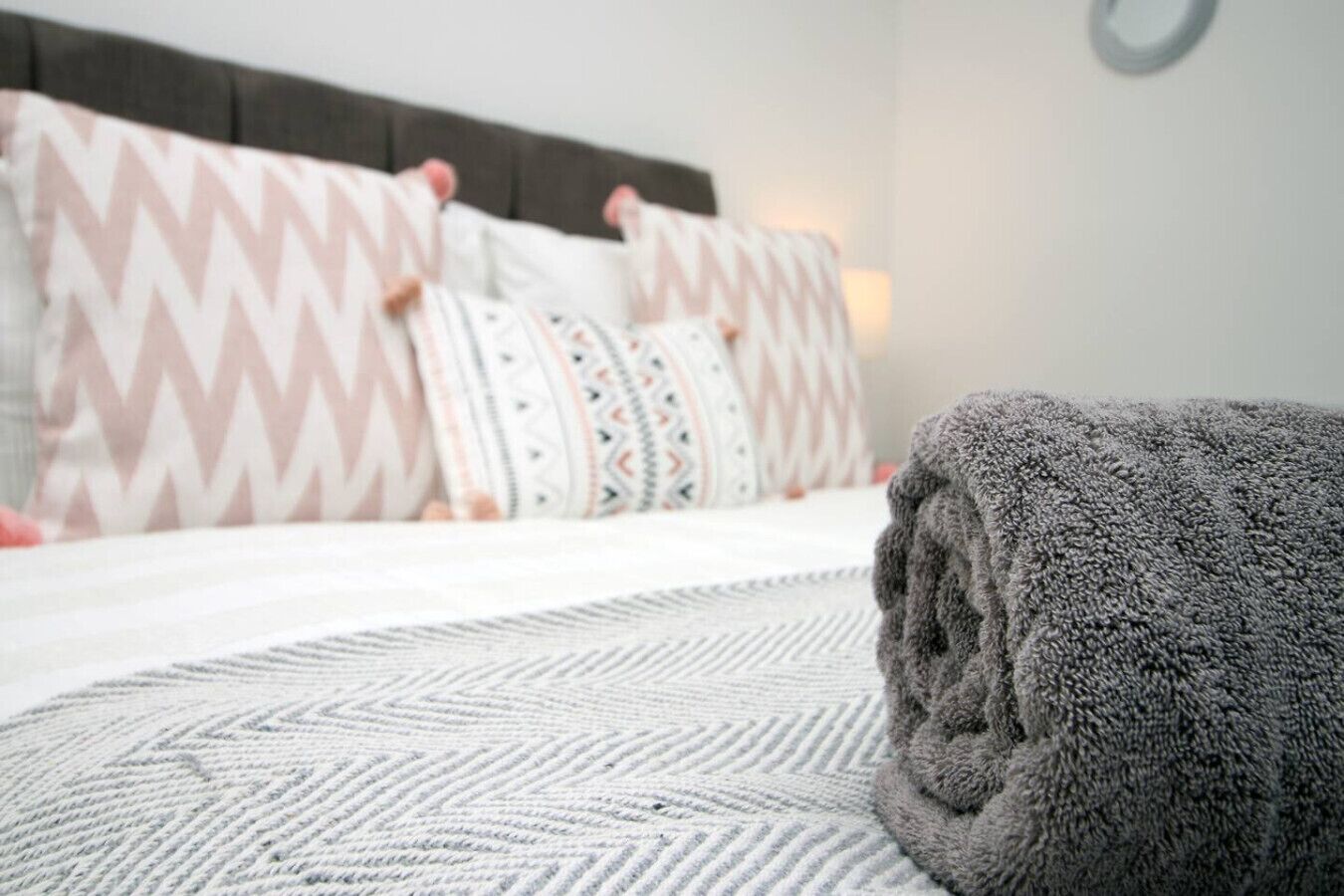 A neatly made bed with patterned pillows and a rolled-up gray towel.