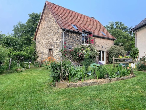 A stone house with a red-tiled roof, a small garden with various plants, and a wooden fence.