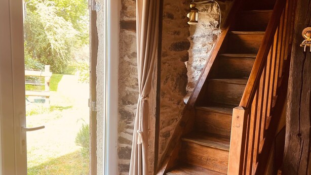 Eine Holztreppe führt zu einer oberen Ebene, eine Steinmauer und eine Tür mit Vorhängen.