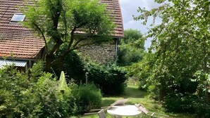 Ein Garten mit einem weißen Tisch und Stühlen, umgeben von üppiger Vegetation und einem Gebäude mit Ziegeldach.