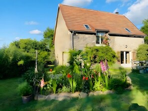 A house with a sloped roof, a visible window, and a garden with various plants.