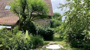 Un jardin avec un bâtiment en pierre, une table blanche avec des chaises et un arbre.