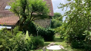 Ein Garten mit Tisch und Stühlen, umgeben von viel Grün und einem Steinhaus mit Ziegeldach.