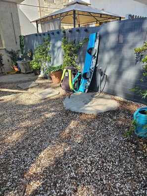 Ein Gartenbereich mit einem Metallzaun, Blumentöpfen, einem blauen Snowboard, das an den Zaun gelehnt ist, und einem Rucksack auf dem Boden.