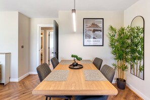 A dining area with a wooden table, four chairs, a bonsai tree centerpiece, and a framed picture on the wall. - St Michaels+View+Lux Coastal Stay+Cinema Lounge (Penzance)