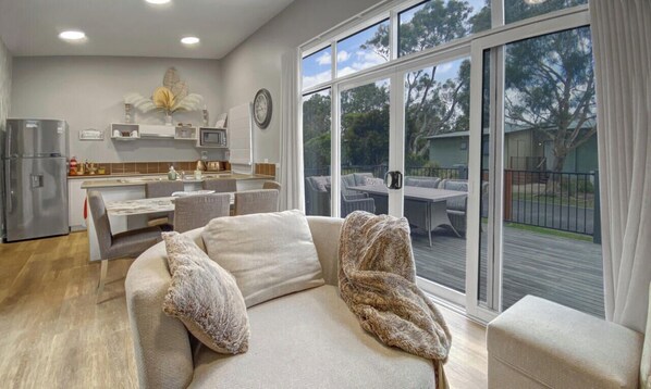 A modern living room with a sofa, a dining table, and a kitchen area. - Island Rose Retreat | Phillip Island Resort Villa (Cowes)