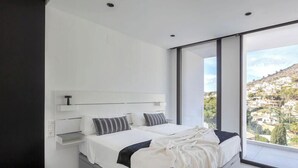 Een moderne slaapkamer met een groot bed, een nachtkastje en uitzicht op een heuvelstad.