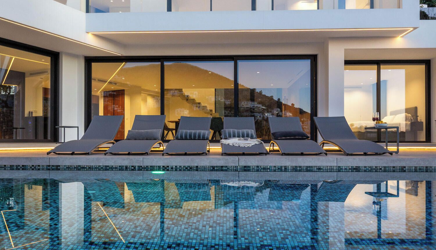 A modern pool area with lounge chairs and a view of a building with large windows.