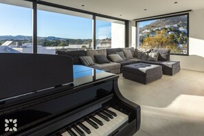 Ein modernes Wohnzimmer mit einem Flügel, einer Eckcouch und großen Fenstern mit Blick auf eine Hügelstadt.
