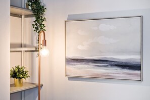 Un interior modern amb un quadre penjat a la paret, una làmpada de peu i una planta en test.