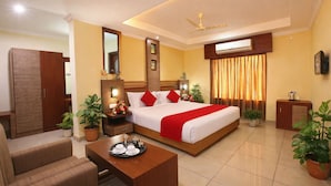 A hotel room with a bed, a desk with a tray of cups, a wardrobe, a mirror, and potted plants. - Hotel Indraprastha Pattazhy (Pathanapuram)