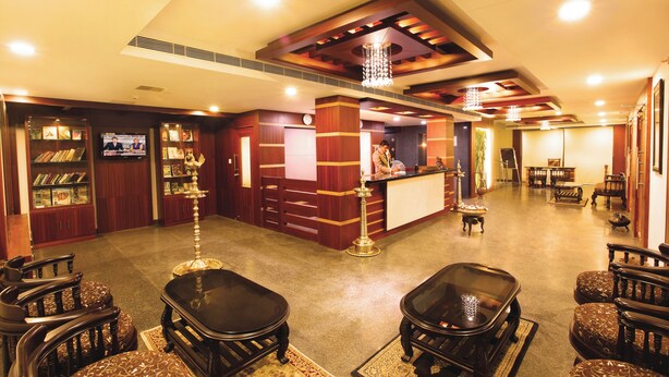 A hotel lobby with a reception desk, seating area, and a bookshelf. - Hotel Indraprastha Pattazhy (Pathanapuram)