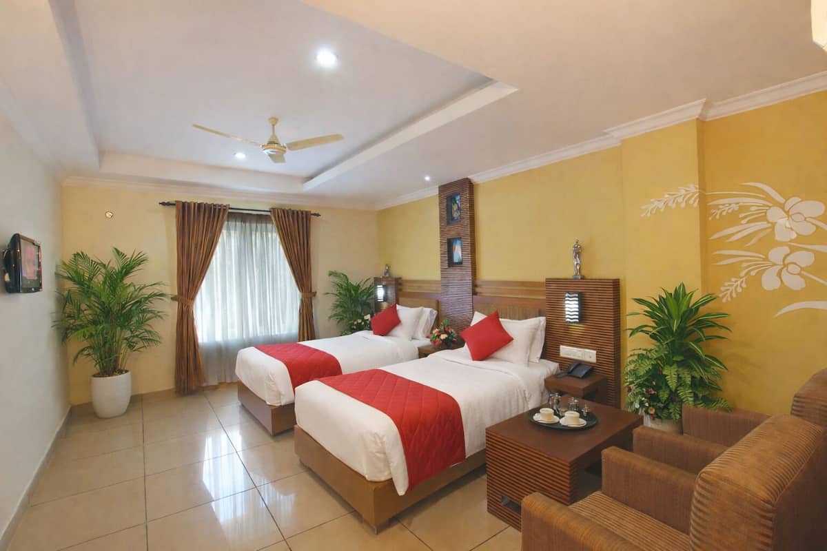 A hotel room with two beds, a ceiling fan, a wooden headboard, a small table with a phone, and two potted plants.