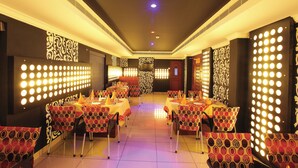 A restaurant with tables and chairs, a patterned wall, and a ceiling with lights. - Hotel Indraprastha Pattazhy (Pathanapuram)