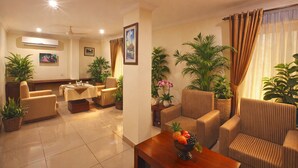 A well-lit living room with a sofa, armchairs, a coffee table, and potted plants. - Hotel Indraprastha Pattazhy (Pathanapuram)