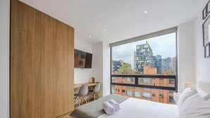 Ein modernes Hotelzimmer mit großem Fenster, Schreibtisch, Stuhl, Bett und an der Wand montiertem Fernseher.