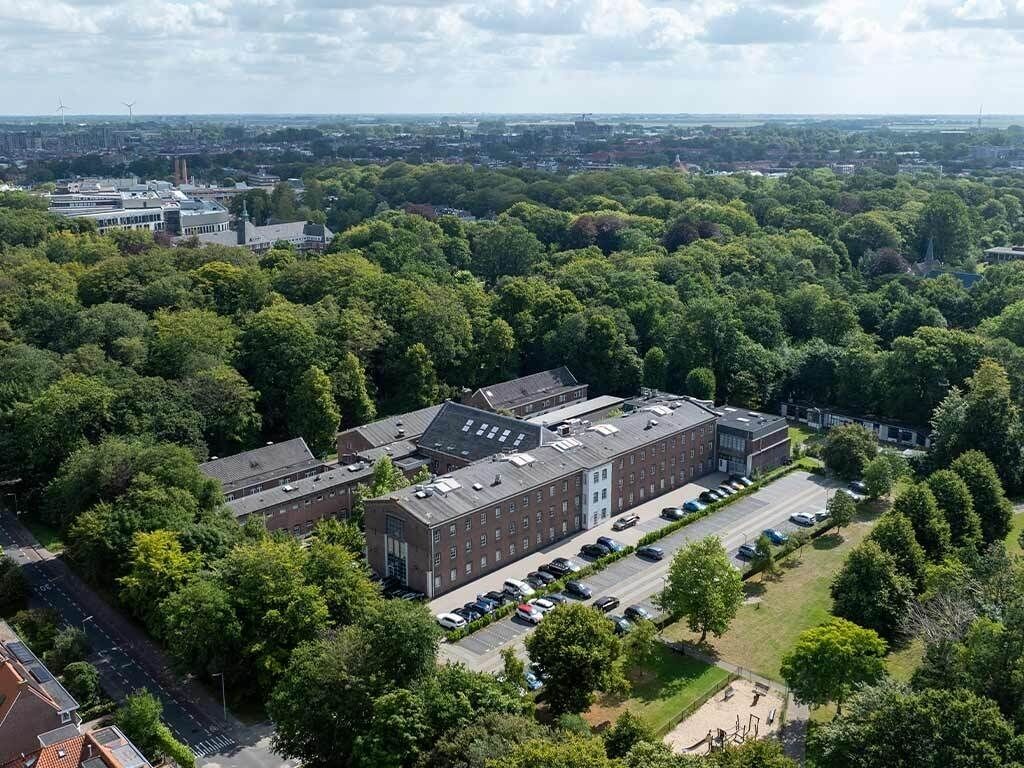 Eine Vogelperspektive eines Campus mit einem großen Gebäude, einem Parkplatz und umliegender Bepflanzung.
