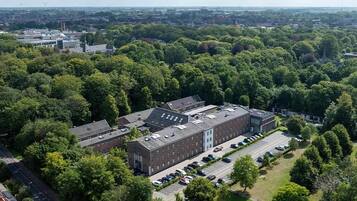 Eine Vogelperspektive eines Campus mit einem großen Gebäude, einem Parkplatz und umliegender Bepflanzung.