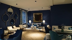 A modern lounge with a blue color scheme, featuring a variety of seating options including armchairs and sofas, a coffee table, and a patterned rug. - Unique Experience in Former Prison Cell (Alkmaar)