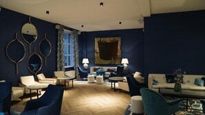 En moderne lounge med blå farvetema, med forskellige siddepladser, herunder lænestole og sofaer, et sofabord og et mønstret tæppe.