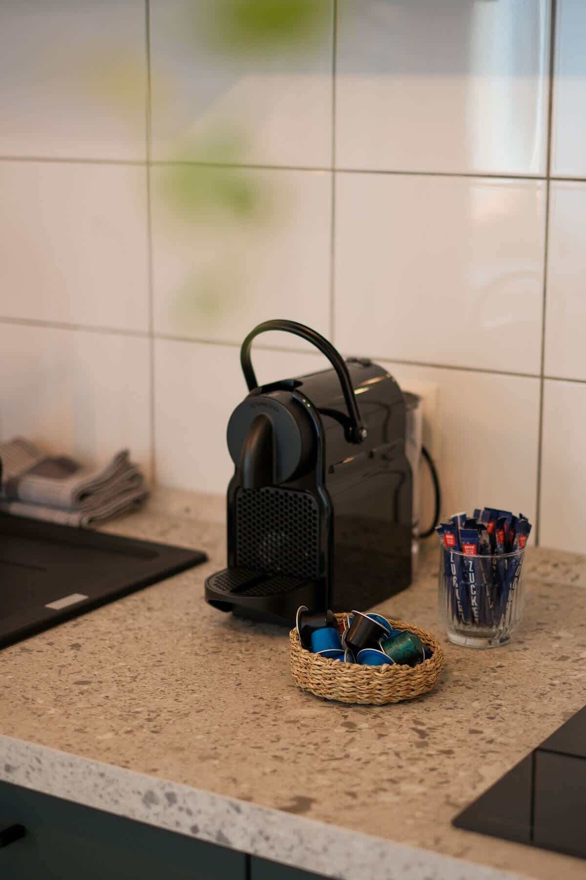 Een aanrecht met een waterkoker, een mand vol bekers en een doosje theezakjes.