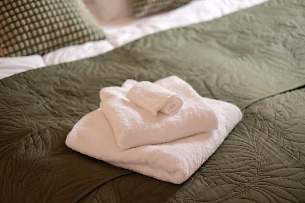Un lit recouvert d’une couverture verte matelassée, avec une serviette blanche pliée posée dessus.