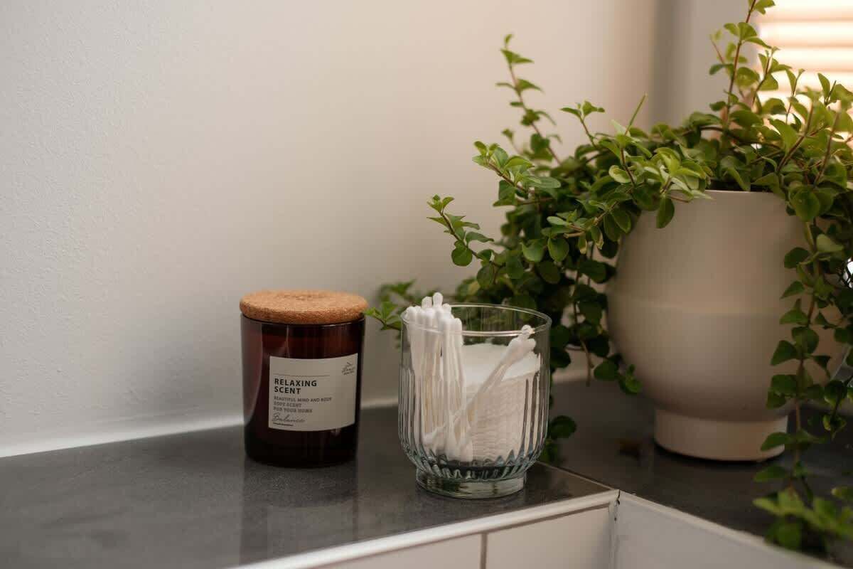 A candle, a glass container with cotton swabs, and a potted plant on a kitchen counter.