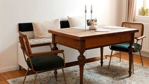 Ein Essbereich mit Holztisch, zwei Stühlen, Teppich und Wandbildern.