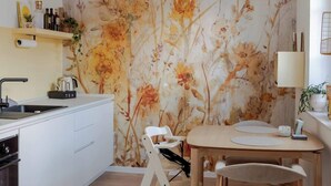 Eine moderne Küche mit weißer Arbeitsplatte, einem Holztisch und floralem Wandpapier.